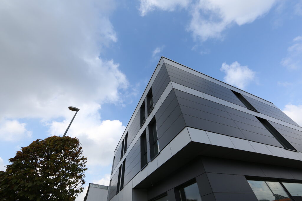Das EconoMy-Hotel ist ein modernes Gebäude mit zweifarbig grauer Verkleidung. Die Außenansicht zeigt die tiefen Fenster der Zimmer.